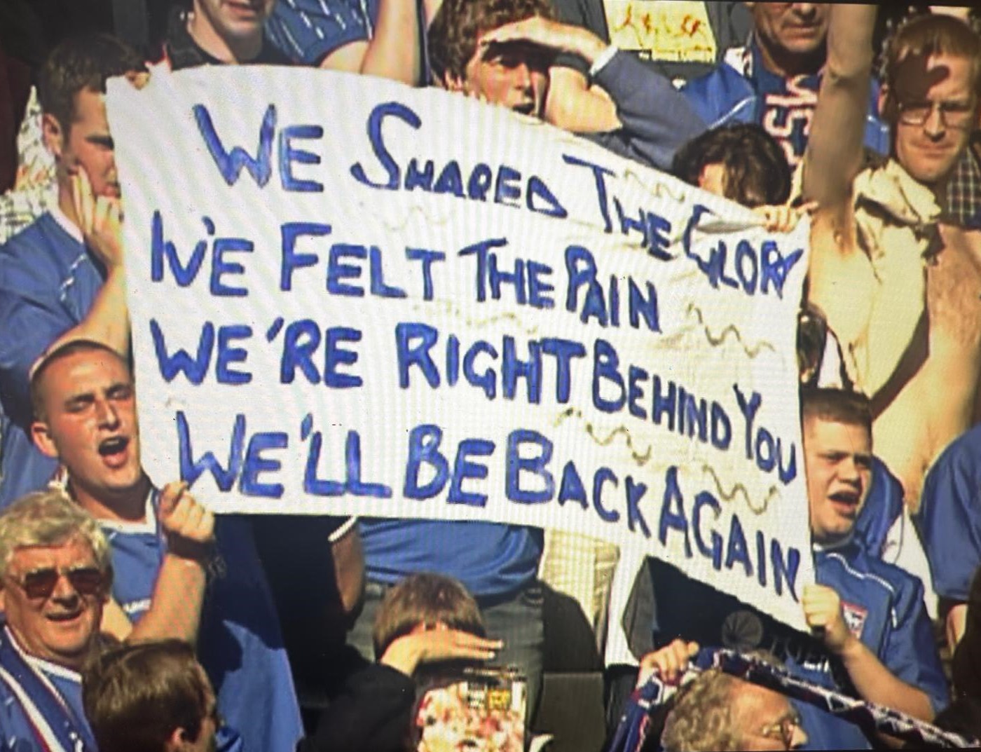 Ipswich Town fans in 2022 holding a banner that reads "We shared the glory, we felt the pain, we're right behind you, we'll be back again""