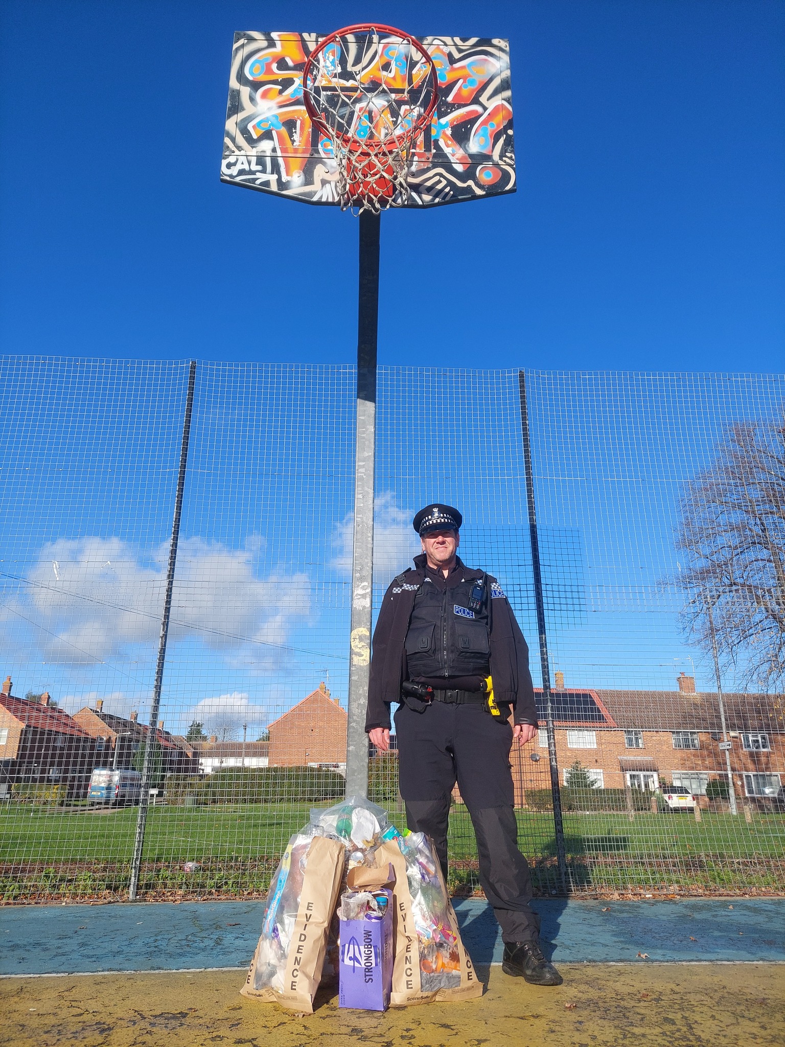 An Ipswich police officer with three evidence bags of rubbish after the clean-up at Hawthorne Drive basketball court in Ipswich