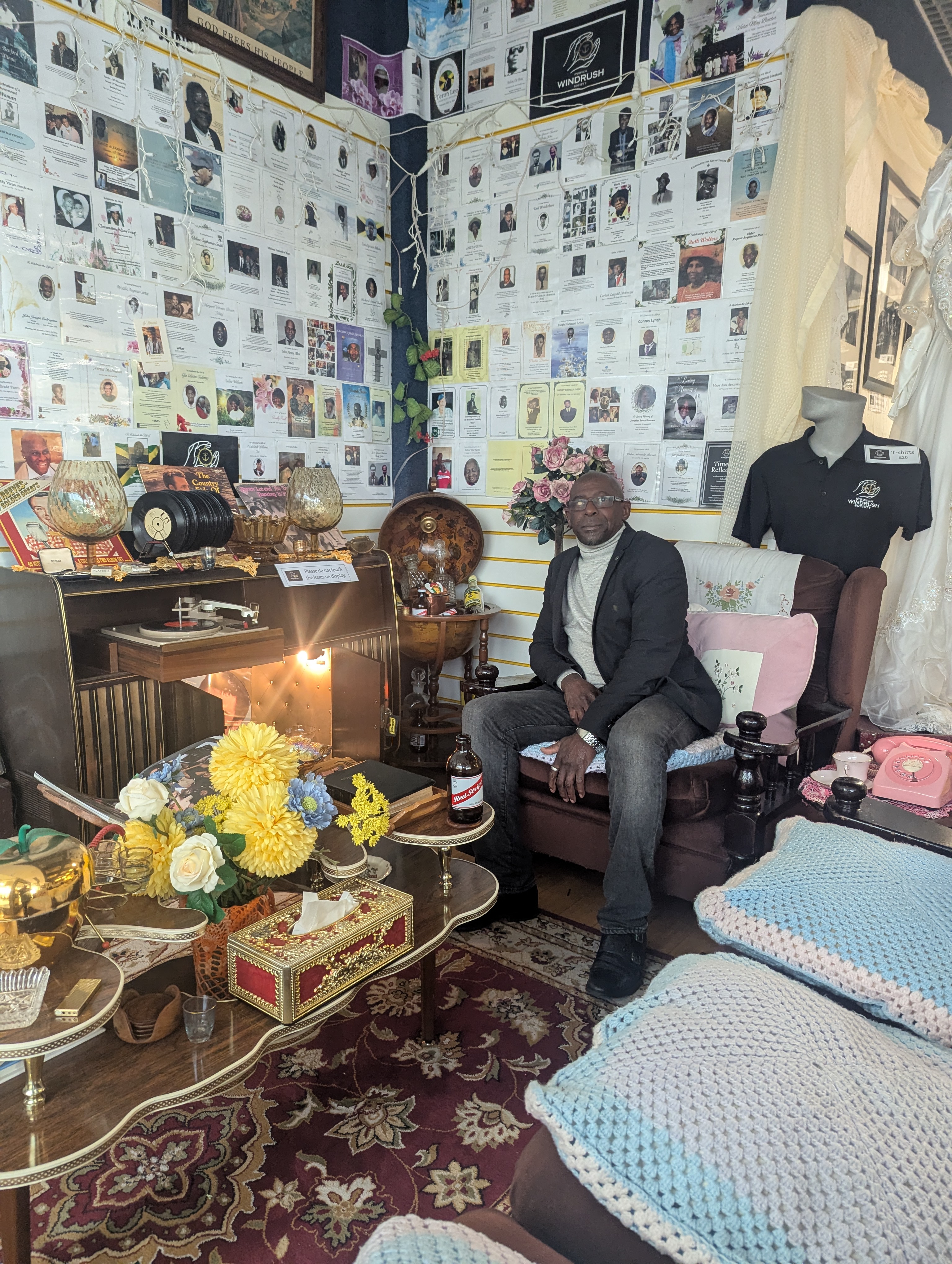 Founder of Ipswich Windrush Society, Max Thomas, seated in the Reflection Room on a sofa, surrounded by cultural artefacts