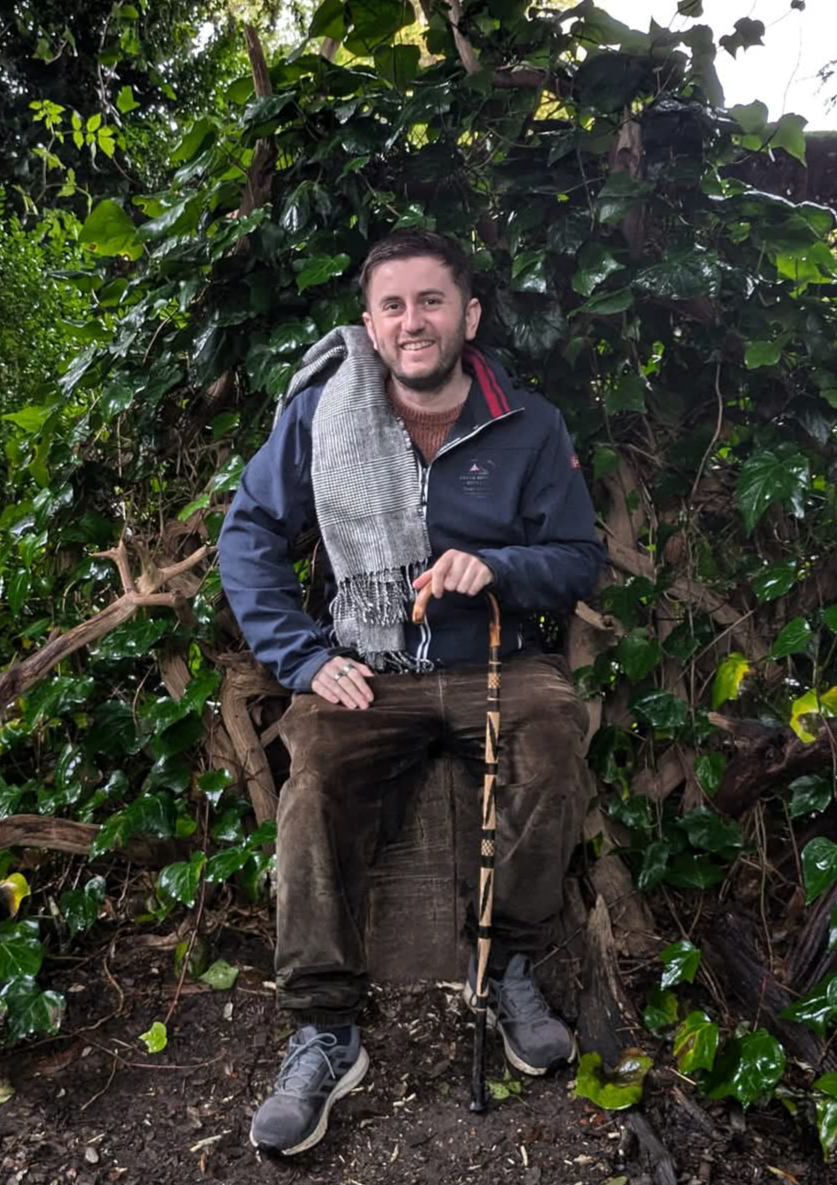 Daniel Lee Harvey, disability activist, seated in nature holding a walking stick