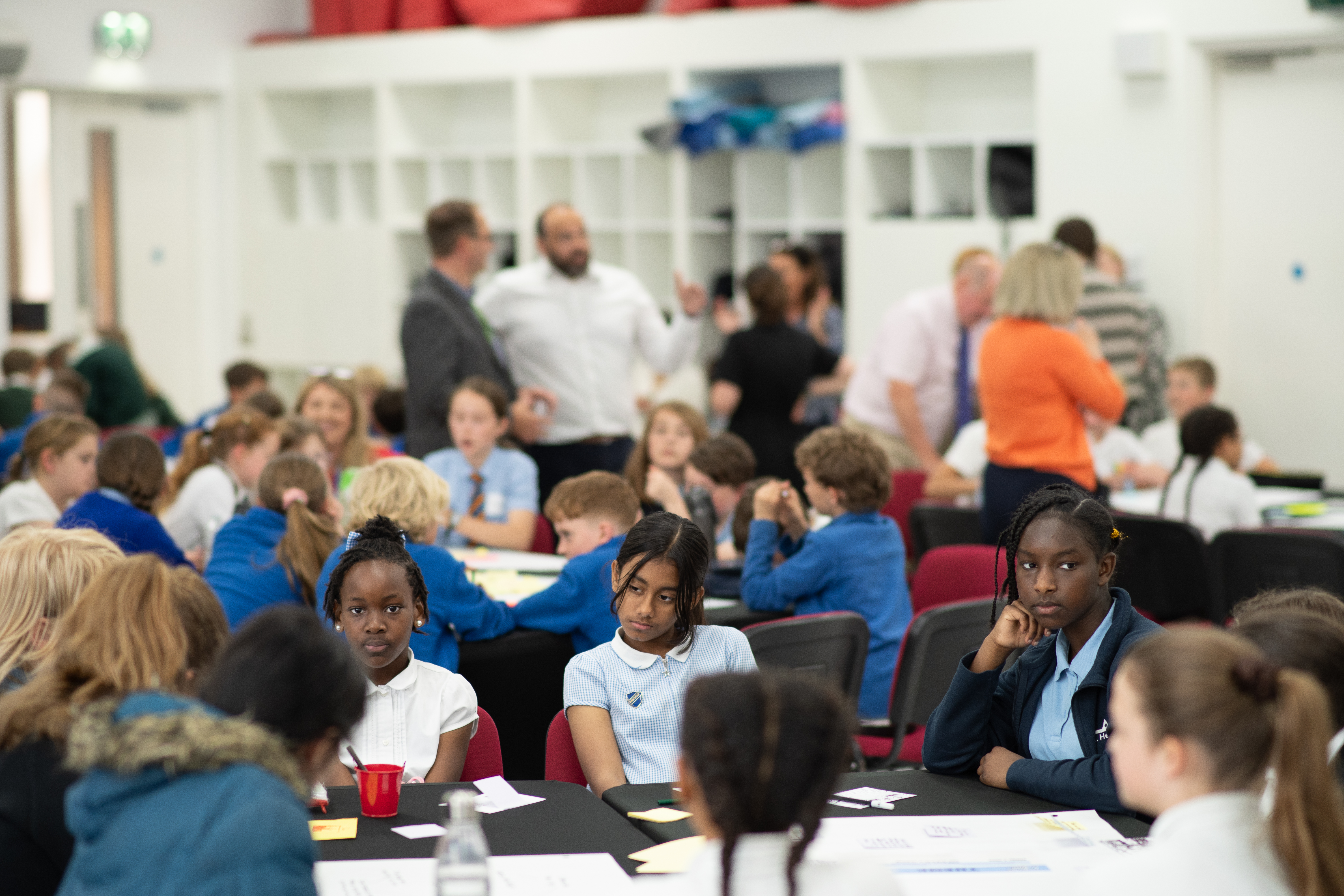 Children in school uniform sit in groups around large tables, focusing on written ideas and discussions during the Hope Hack