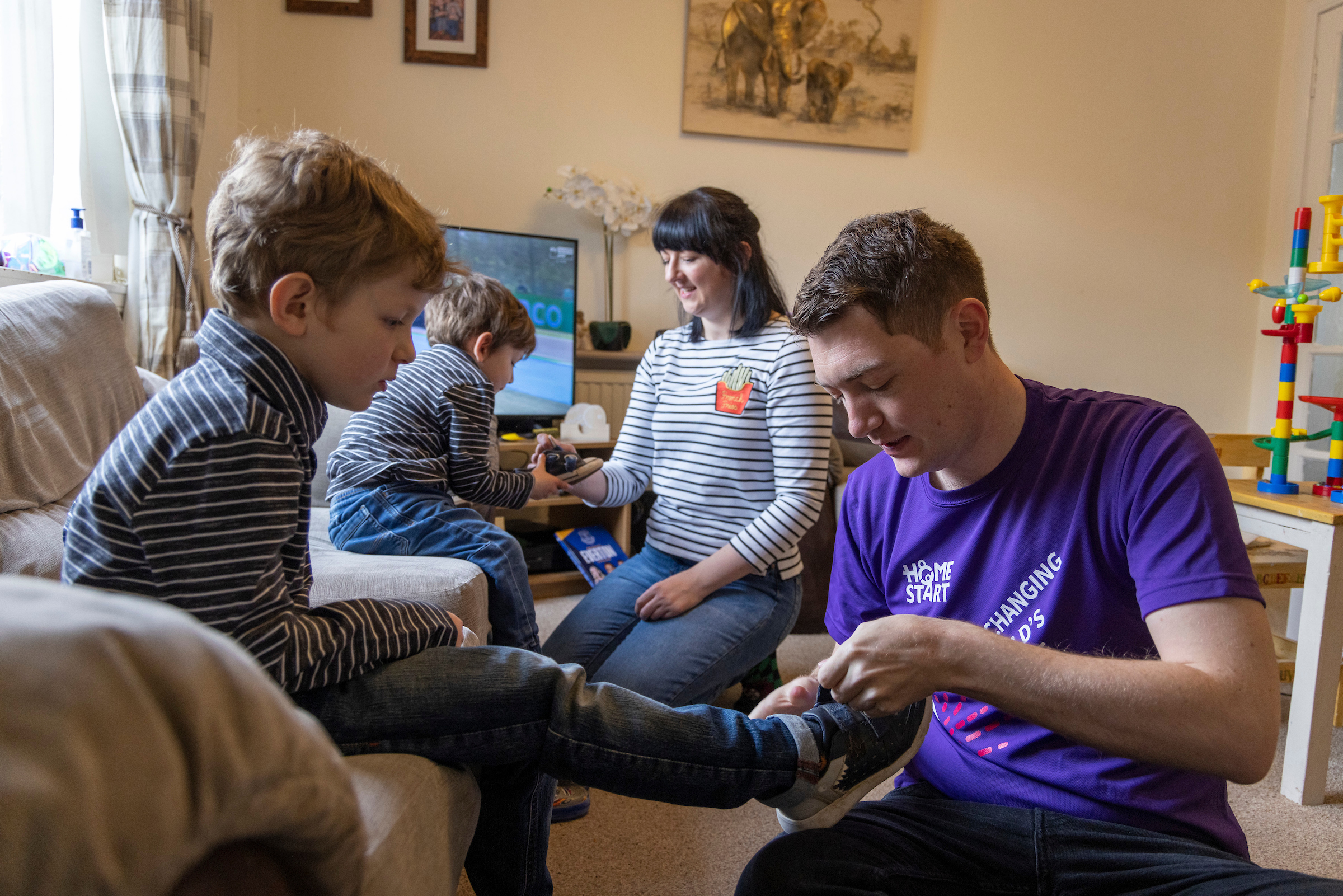 Young male Home-Start volunteer helps put shoes on children