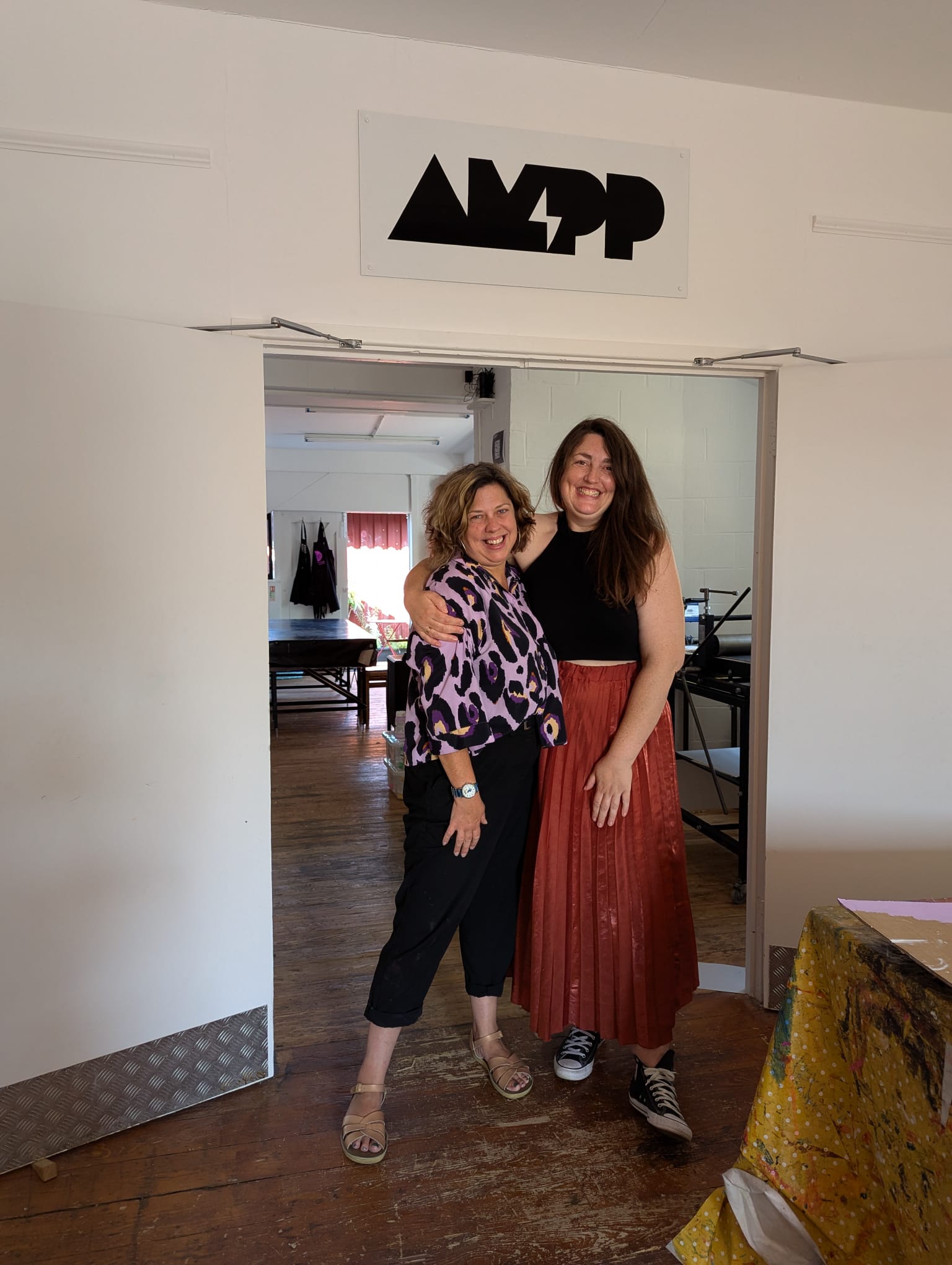 The two founders oc AMPP studio stand in front of a sign