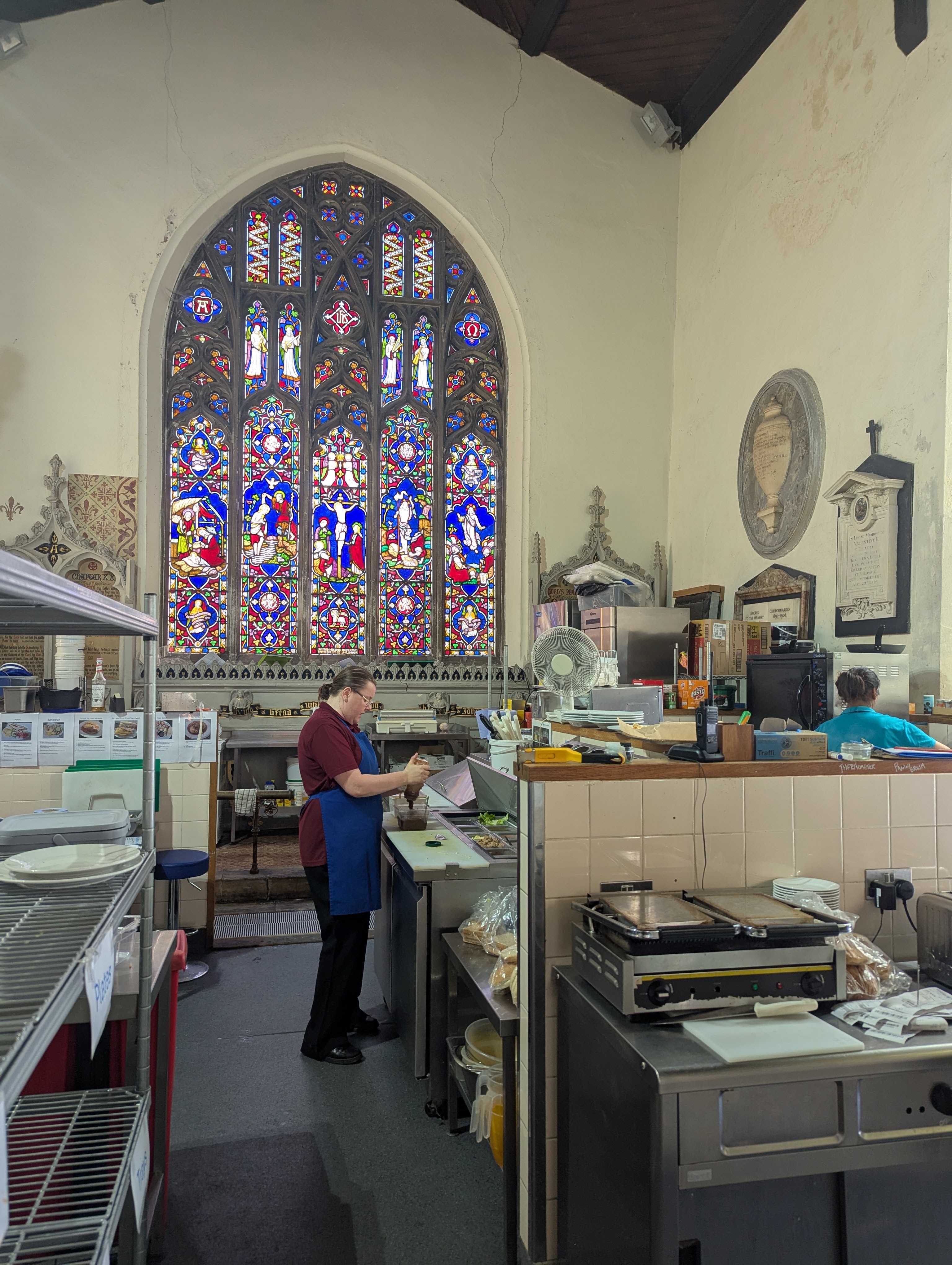 Staff member working in the kitchen at St Lawrence Café with large stained-glass windows filling the background
