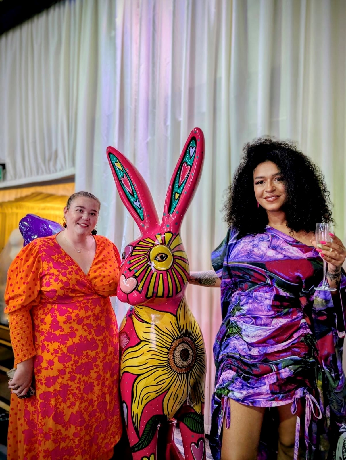 Two women standing next to a brightly painted hare sculpture with hearts and flowers, at the St Elizabeth Hospice art trail auction