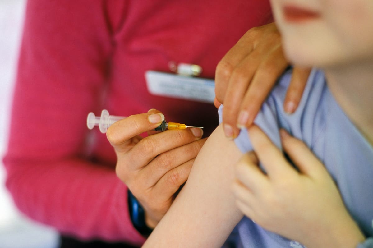 A child about to be given the MMR (mumps, measles, rubella) vaccination into their arm by a surgery nurse
