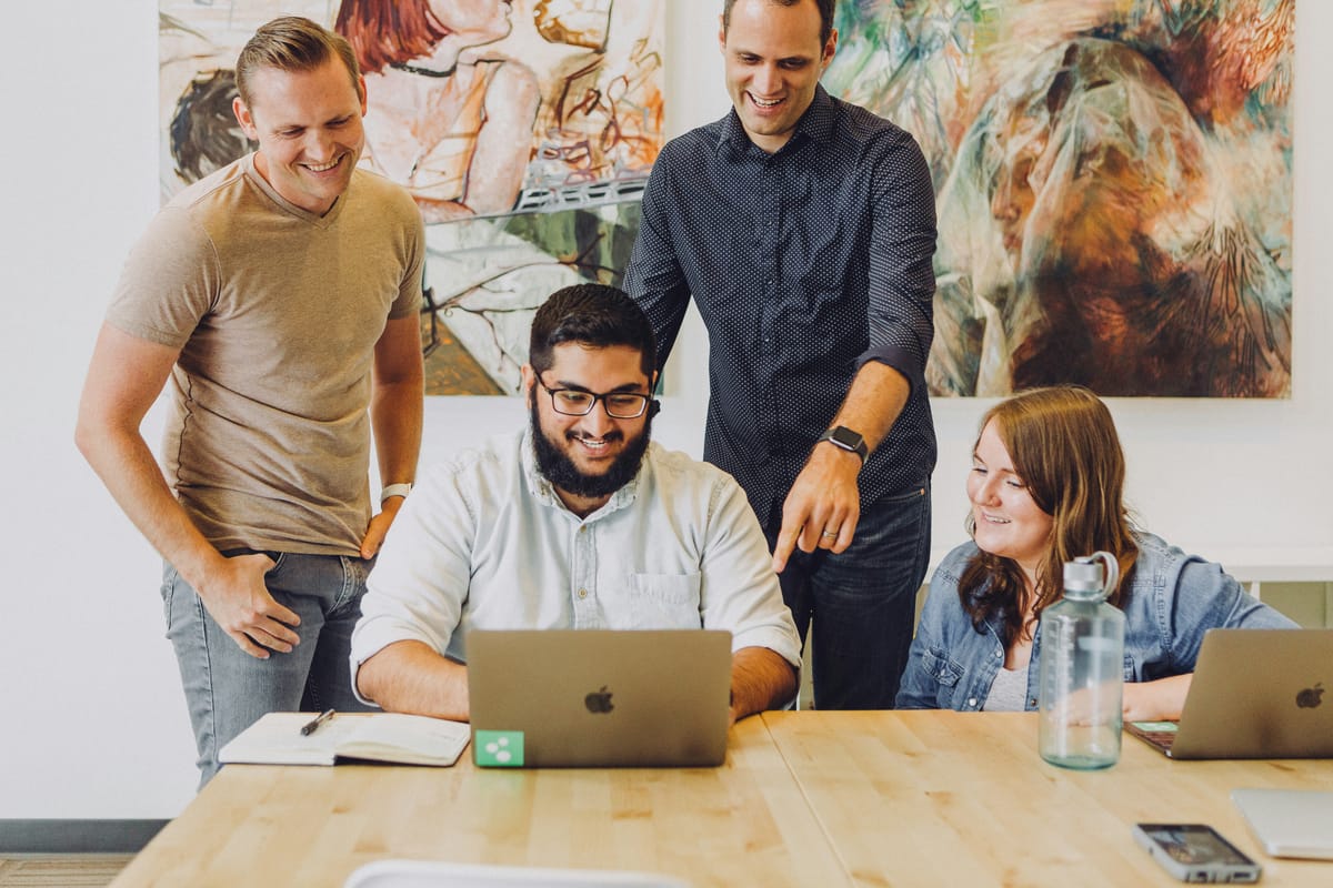 A group of colleagues gathered around a laptop in the office