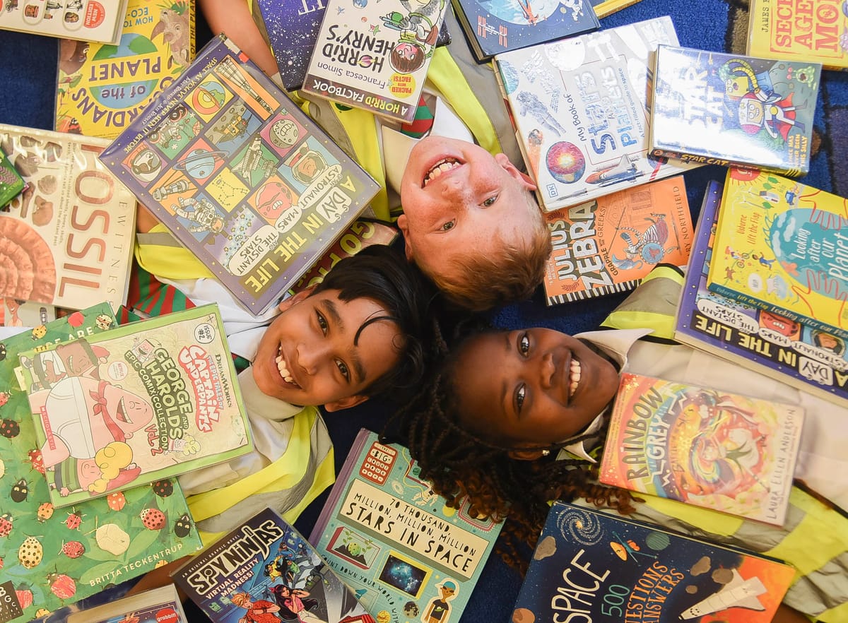 Three children lying on the floor of a library covered with books
