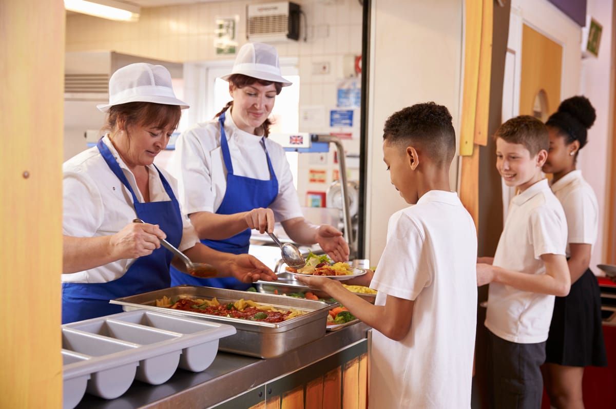 Two women serving food to a boy in a school cafeteria