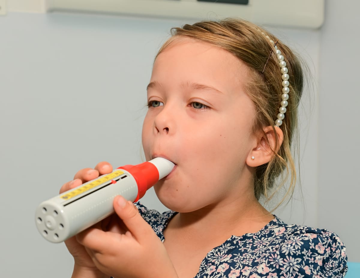 Child holding a peak flow meter to her mouth, blowing into it as part of an asthma check